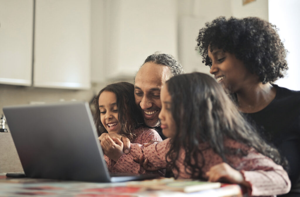 Planejamento financeiro para comprar um imóvel. Família brasileira sentada em frente a mesa, olhando para um notebook, dentro de casa.