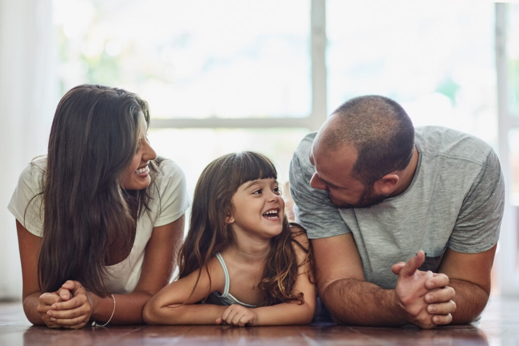 Momento ideal para comprar um imóvel. Foto de família de três integrantes, deitados no chão lado a lado: mãe, pai e filha criança.
