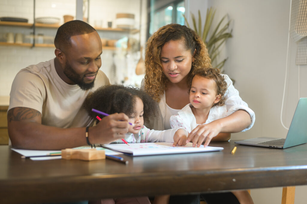 O que é ITBI?Família negra sentada em volta de mesa dentro de casa, um homem, uma mulher adultos e duas criancas.