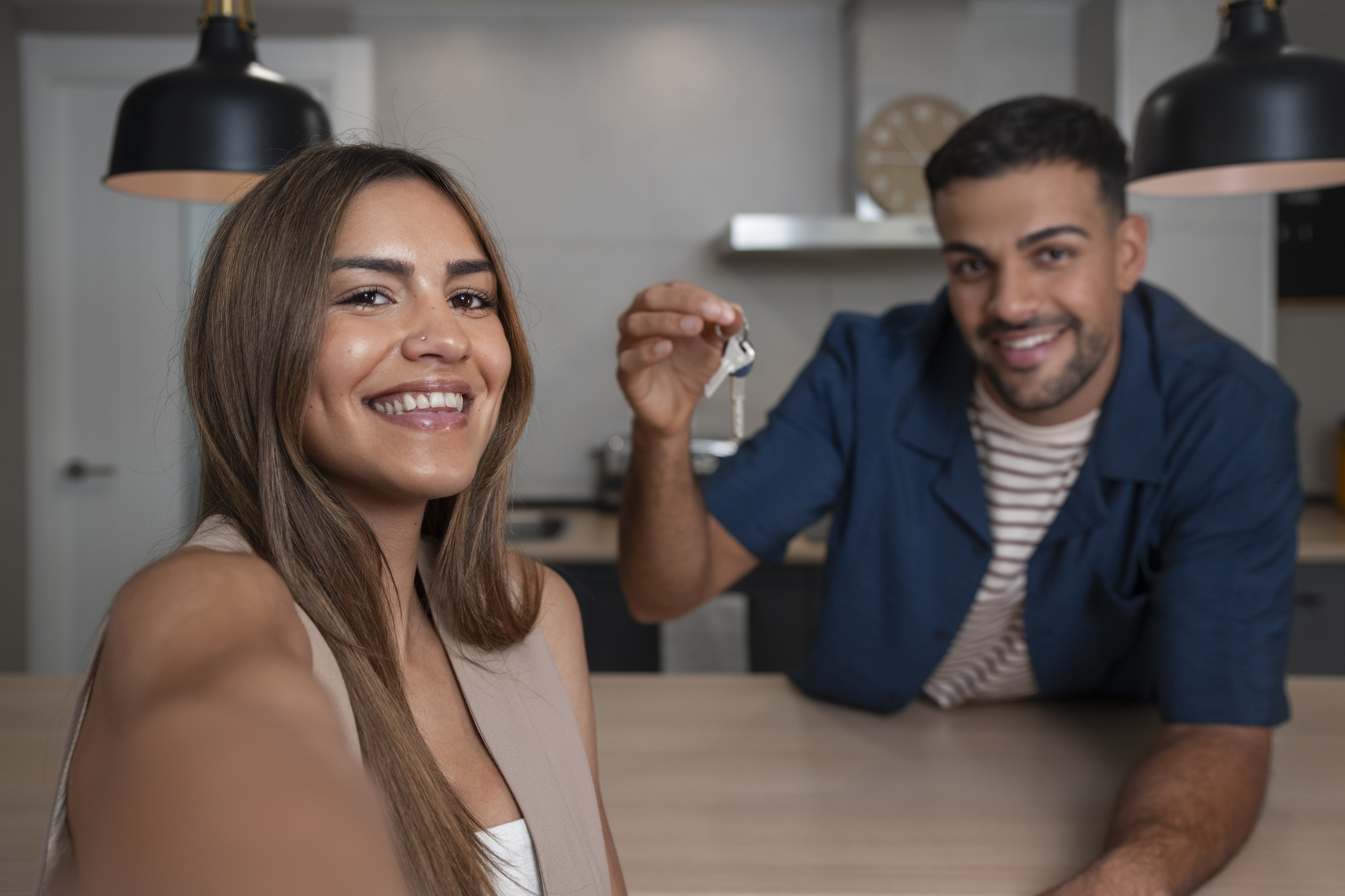 Valorização de imóvel. Em ambiente interno, casal, homem e mulher, sorriem para a câmera. Homem segura a chave da casa própria, ambos felizes.